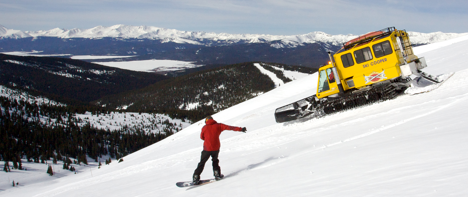 snowboarder and snowcat heading down the slope