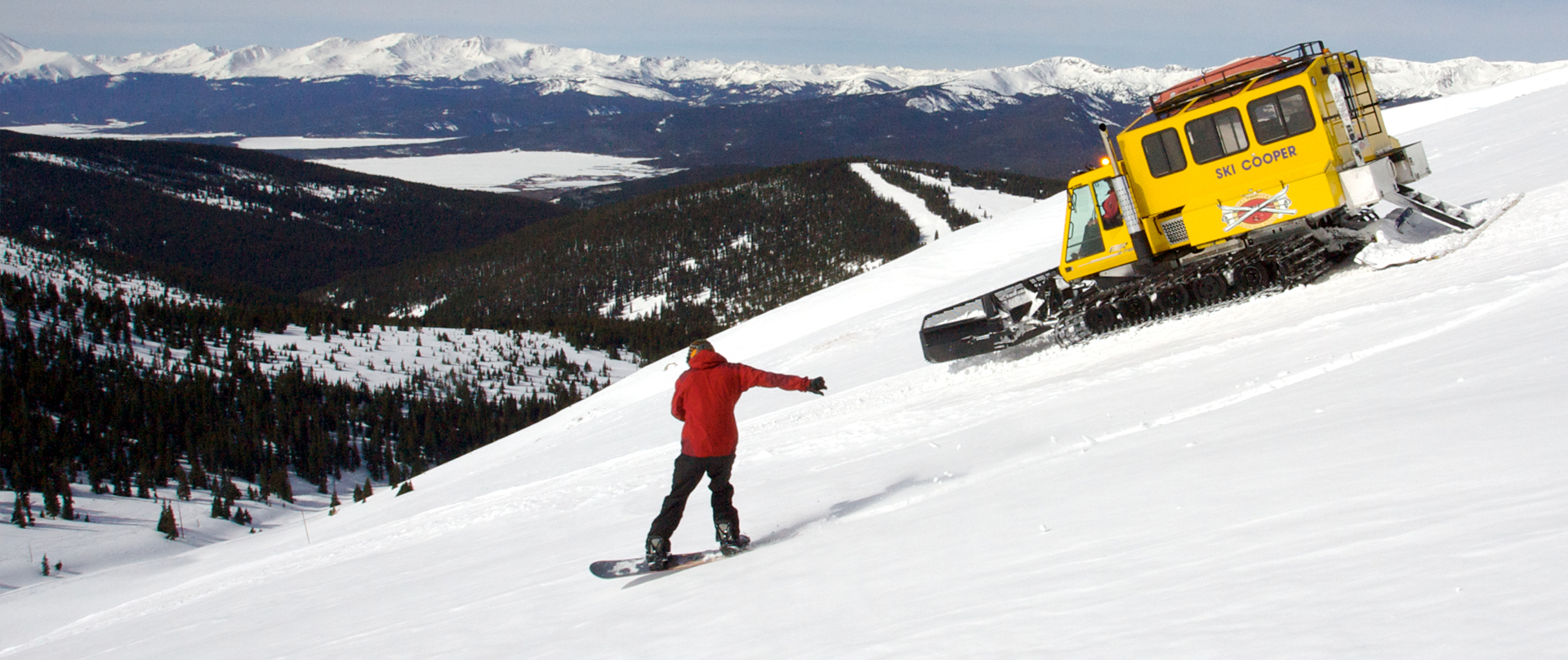 Snowboarder and Snowcat heading down the slopes